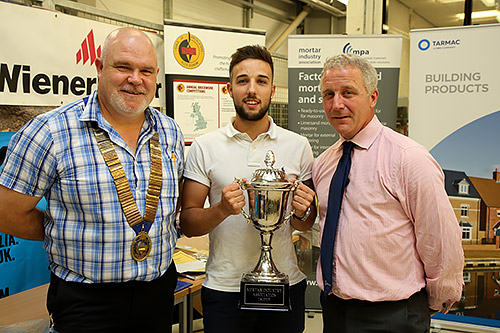 Tyler Pearce of Brooklands College receives the MIA cup for winning the senior section of the Guild of Bricklayers national 2017 competition from guild president, Phil Vine Roberts ( left) and Tarmac Building Products’ Iain Betts.